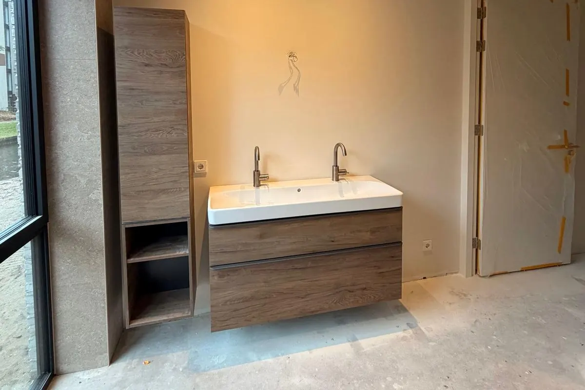 Badkamer met dubbele wastafel, hoge kast en groot raam tijdens de afbouw