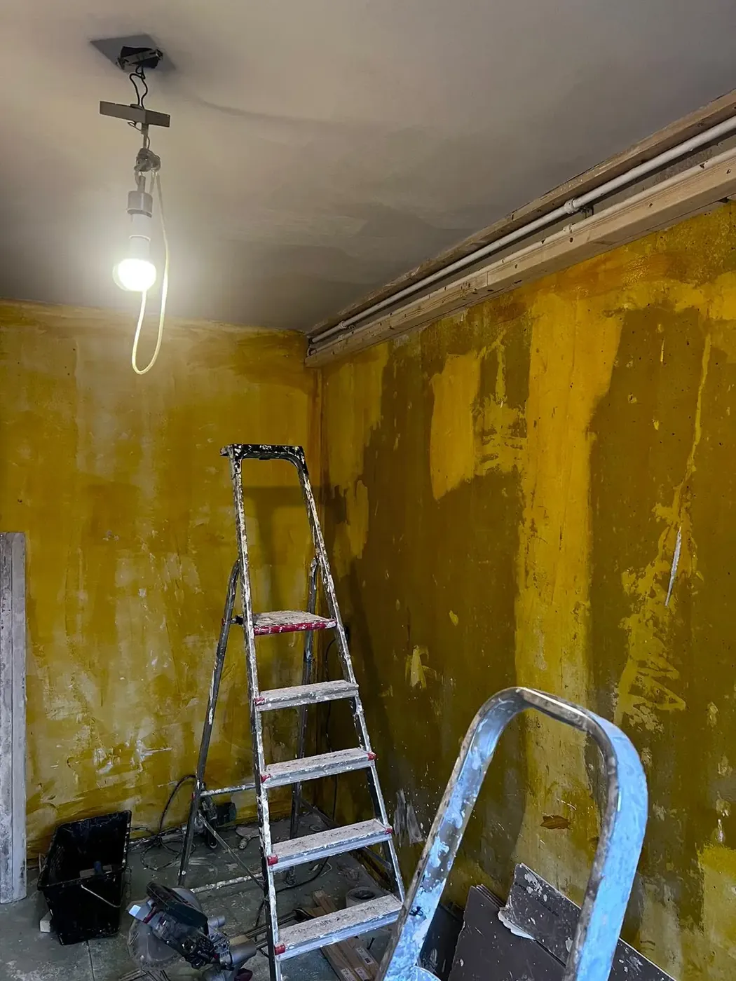 Kamer vóór het stucwerk: kale, vervuilde muren met een trapleer